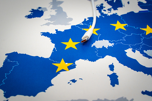 USB-C cable over an european map with the EU flag symbolizing the Common charger directive. In 2024, a USB-C port will become mandatory for a whole range of electronic devices such as mobile phones, tablets, and headphones. Laptops will also be covered by the new rules