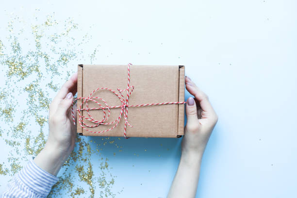istock Hands holding a craft gift. Christmas gift on a blue background. Gift with red and white rope 1495679620