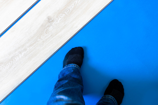 High angle view of a person standing on blue foam flooring underlayment next to laminate floor planks