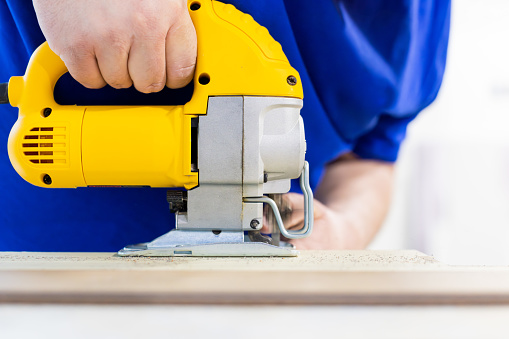 A homeowner is using a jig saw to make a complex cut of a laminate floor plank