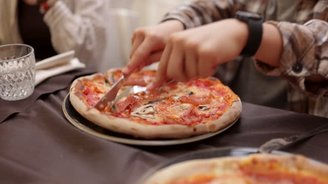 Teenage kids enjoying eating fresh pizzas in Italian restaurant.