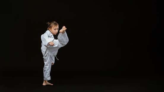 Banner: Asian-Australian girl poses in martial arts Practice taekwondo, karate, judo against a dark background in the studio. Asian kids karate or Taekwondo martial arts. Sport kid training action.