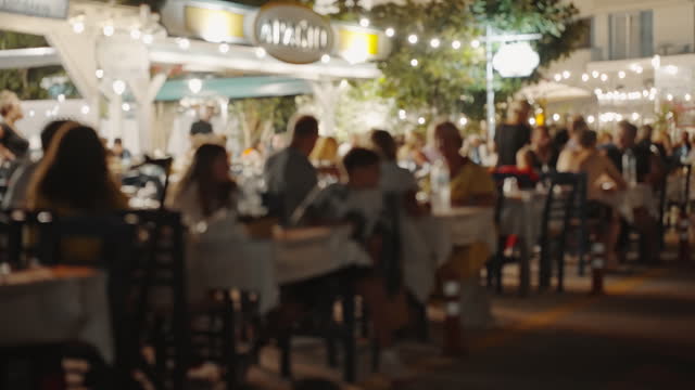Blurred of interior of large beautiful restaurant with bright lighting. Waitress comes to table, gives visitors menu and goes for drinks. Defocused interior and restaurant visitors. Lifestyle