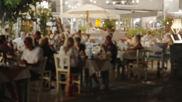 Defocused interior and restaurant visitors. Lifestyle. Blurred of interior of large beautiful restaurant with bright lighting. Waitress comes to table, gives visitors menu and goes for drinks
