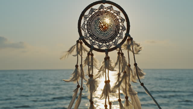 Silhouette Indian talisman symbol. Boho style. Dreamcatcher golden disk sun slow motion close up on background of blue sea sky in rays of sun at dawn in summer.