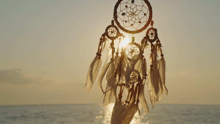 Silhouette Indian talisman symbol. Boho style. Dreamcatcher golden disk sun slow motion close up on background of blue sea sky in rays of sun at dawn in summer.