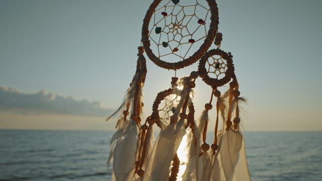 Silhouette Dreamcatcher golden disk sun slow motion close up on background of blue sea sky in rays of sun at dawn in summer. Indian talisman symbol. Boho style