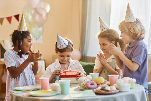 Diverse group of happy children at Birthday party with little boy opening presents