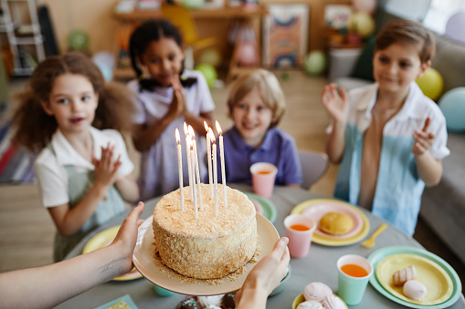 High angle close-up of mother bringing birthday cake with candles to children during birthday party, copy space