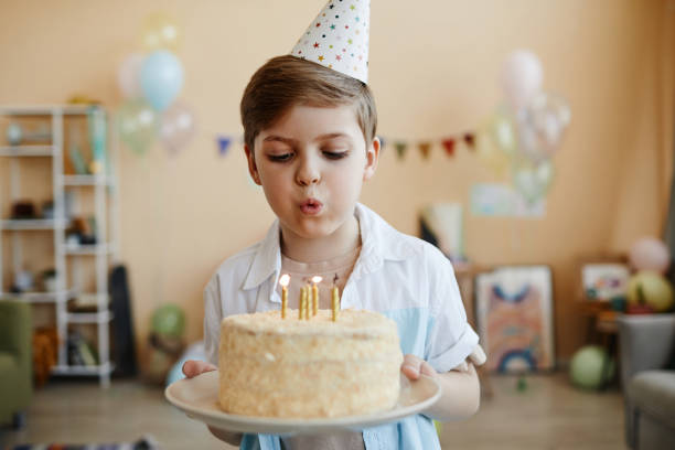 istock Cute boy holding birthday cake and blowing candles 1495695045