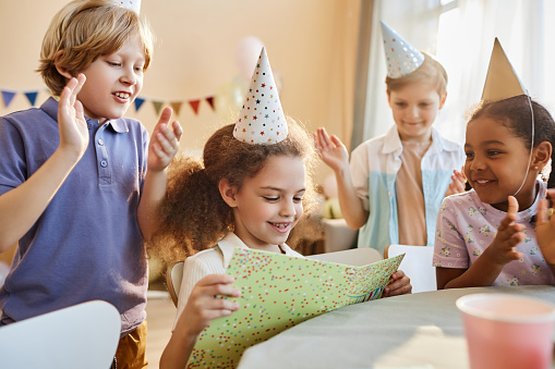 Diverse group of happy children at Birthday party with cute girl opening presents