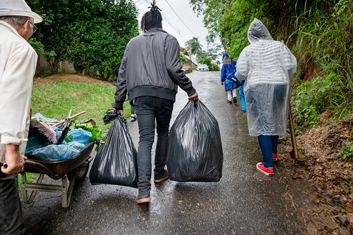 Rear view of a group of people walking with bags full of garden refuse up a driveway in the rain
