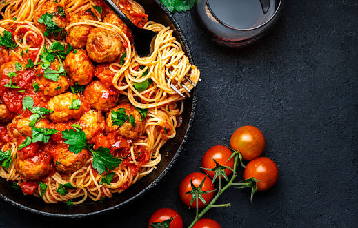 Prepared spaghetti pasta with fried pork meatballs in tomato sauce with parsley in frying pan, black table background, top view