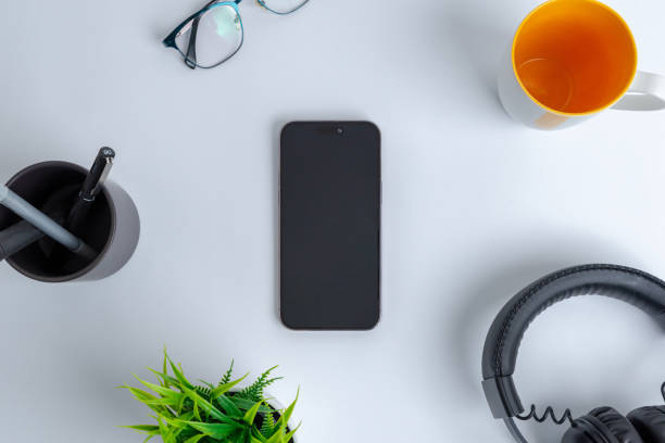 istock Phone on work desk. Top view, flat lay composition. Surrounded by coffee mug, headset, plant, glasses and pens 1495713866