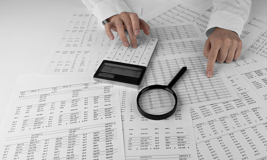Accountant holding a calculator pointing at numbers on financial documents. Ð¡oncept of finance, search and accounting.