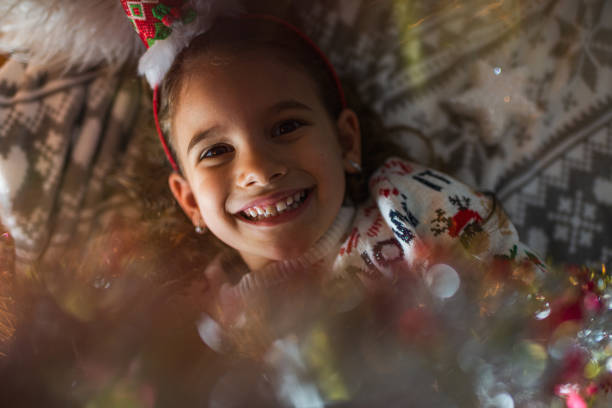 Christmas holiday concept. Toddler girl wearing Santa Claus hat and christmassy dress making funny face sticking tongue out.