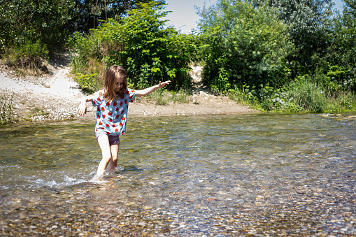 Caucasian child girl wading a clear stream on a bright sunny day. Parco del Ticino, Lombardy, Italy.