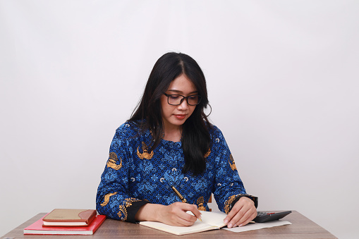 Asian female in batik korpri, indonesian traditional worker uniform writing something on a book