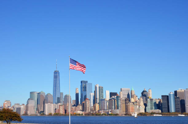 a bandeira americana e o rio hudson e manhattan ao fundo durante o dia - ilha ellis - fotografias e filmes do acervo