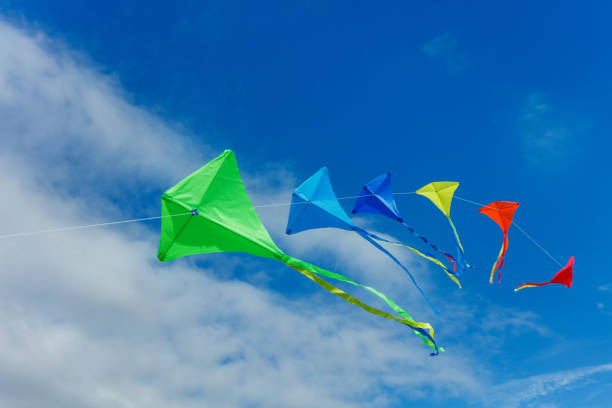 Group of many beautiful color kites fly on the string over blue sky with clouds