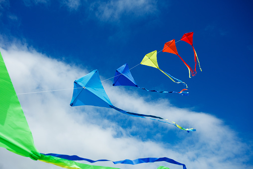 Large group of many beautiful colorful kites fly on the string over blue sky with clouds