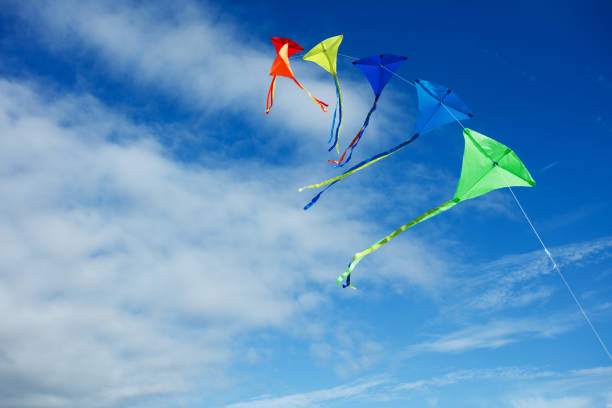 Group of many beautiful colorful kites fly on the string over blue sky with clouds