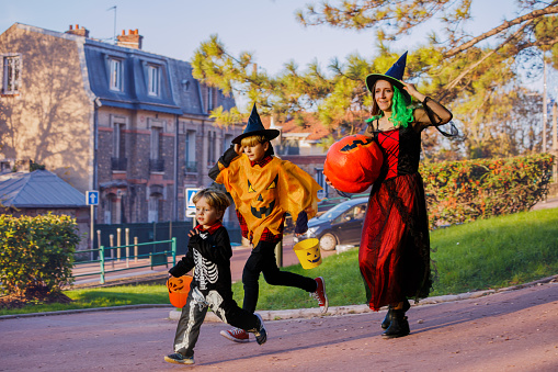Family with brother boys run in Halloween disguise hold bucket for candies over the town street side view action portrait