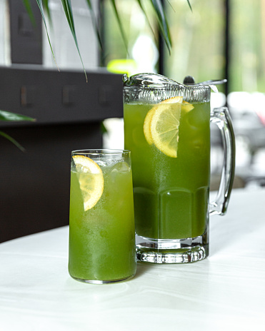 Jug and glass of green lemonade with lime and lemon