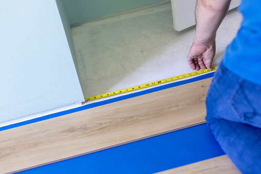 A homeowner measuring floor with tape measure to install flooring underlayment