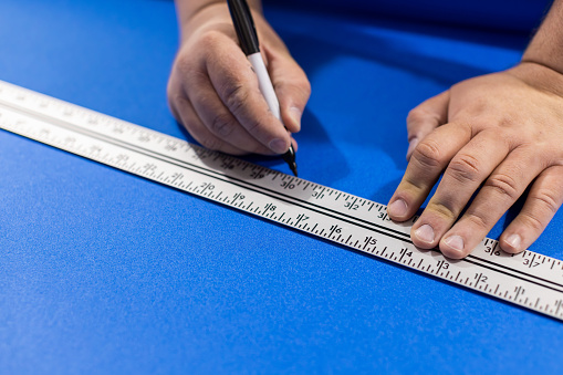 A homeowner is using a ruler and a felt tip pen to measure and mark a piece of flooring underlayment to cut