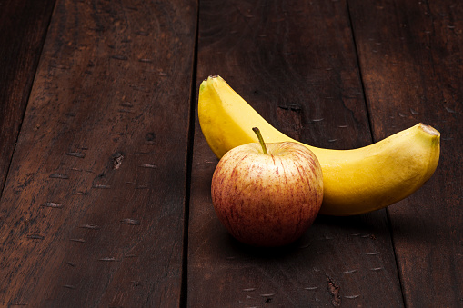 Still life of one red apple fruit and one banana on rustic wooden table in the kitchen at home.