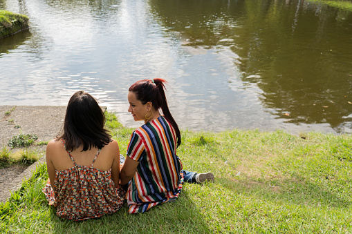 two women sitting back to back in a meadow on the edge of a side chatting and smiling