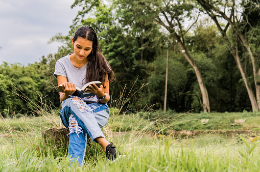 Young Woman Practicing Reading while sitting in the meadow at sunset