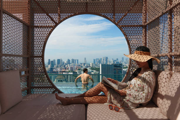 Asian man on holiday enjoying the city skyline from the hotel's rooftop infinity pool stock photo