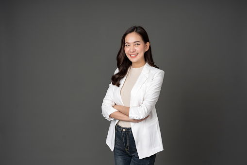 Asian female executive with long hair She smiled brightly and confidently stood with her arms crossed. She wore a white suit. and stand to take pictures with a gray scene in the studio