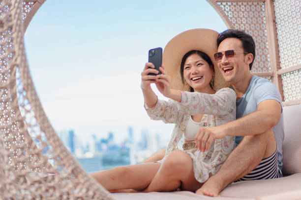Happy Asian couple on holiday taking a selfie together by the poolside Asian couple on holiday taking a selfie together by the poolside singapore happy people stock pictures, royalty-free photos & images