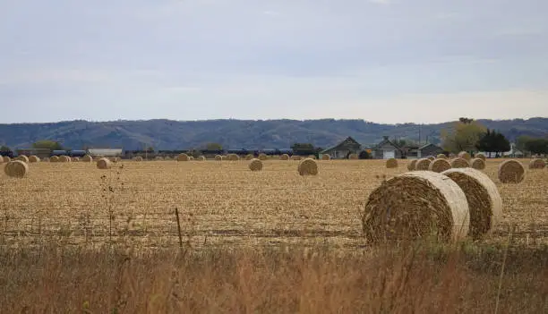 The landscape of rural Iowa with an old schoolhouse, a train passing through, and bales of hay