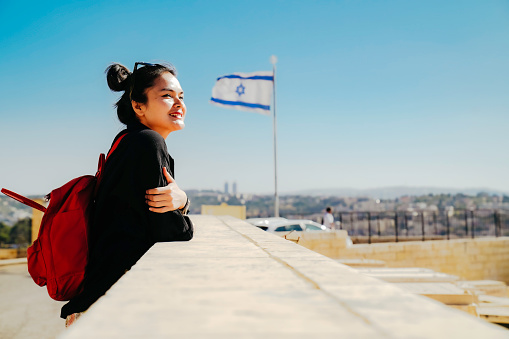 asian woman standing at The Old Town with the Dome of the Rock at the sunset from Mount of Olives