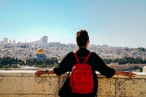 asian woman standing at The Old Town with the Dome of the Rock at the sunset from Mount of Olives