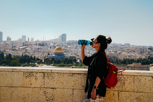 asian woman standing at The Old Town with the Dome of the Rock at the sunset from Mount of Olives
