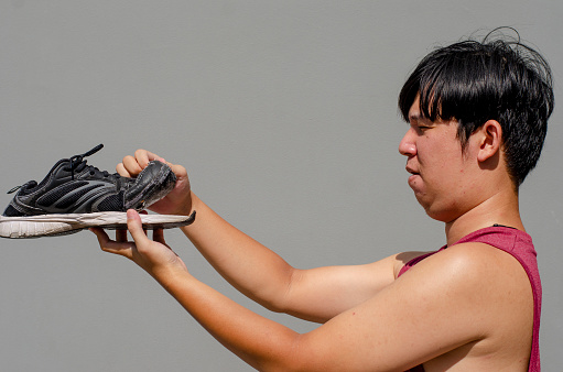 Caucasian Asian man holding old torn black sneakers with in front of shoes.