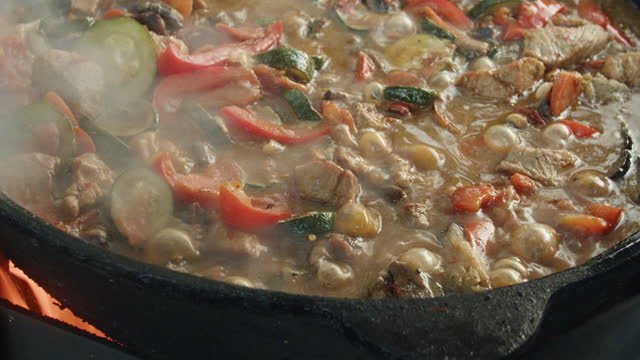 Stewing vegetables with meat in a cauldron over an open fire.