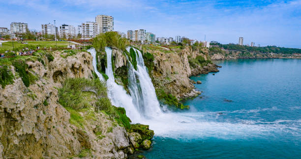The more famous Karpuzkaldiran Lower Düden Waterfall roars down into the sea from the 50 m high cliffs in Antalya Lara district.
The Düden river falls from the 40 meter high cliffs of Antalya by the sea for the second time, creating the picturesque natural spectacle. The force of the falling water is noticeable in the cool draft around the waterfall. You can even feel it on the top of the cliffs. cascada duden cayendo en el mar mediterráneo en antalya, lara antalya en un día soleado y brillante, cascadas lower duden, cascada alta que se vierte en el mar, la cascada en la ciudad cae al mar, el famoso destino turístico de turquía, el agua más al