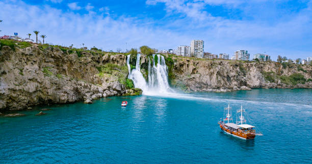 The more famous Karpuzkaldiran Lower Düden Waterfall roars down into the sea from the 50 m high cliffs in Antalya Lara district.
The Düden river falls from the 40 meter high cliffs of Antalya by the sea for the second time, creating the picturesque natural spectacle. The force of the falling water is noticeable in the cool draft around the waterfall. You can even feel it on the top of the cliffs. cascada duden cayendo en el mar mediterráneo en antalya, lara antalya en un día soleado y brillante, cascadas lower duden, cascada alta que se vierte en el mar, la cascada en la ciudad cae al mar, el famoso destino turístico de turquía, el agua más al