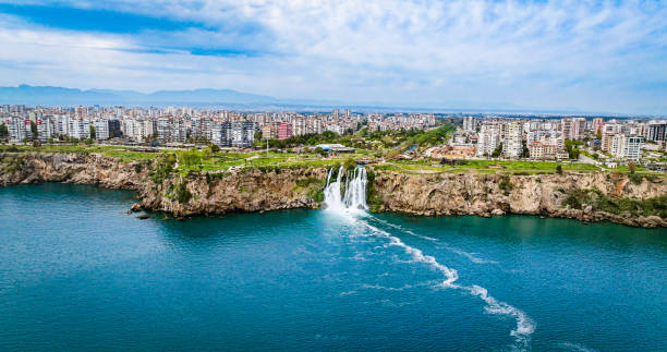 The more famous Karpuzkaldiran Lower Düden Waterfall roars down into the sea from the 50 m high cliffs in Antalya Lara district.
The Düden river falls from the 40 meter high cliffs of Antalya by the sea for the second time, creating the picturesque natural spectacle. The force of the falling water is noticeable in the cool draft around the waterfall. You can even feel it on the top of the cliffs. cascada duden cayendo en el mar mediterráneo en antalya, lara antalya en un día soleado y brillante, cascadas lower duden, cascada alta que se vierte en el mar, la cascada en la ciudad cae al mar, el famoso destino turístico de turquía, el agua más al