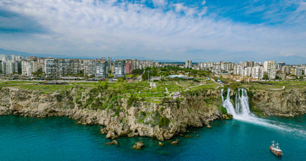 The more famous Karpuzkaldiran Lower Düden Waterfall roars down into the sea from the 50 m high cliffs in Antalya Lara district.
The Düden river falls from the 40 meter high cliffs of Antalya by the sea for the second time, creating the picturesque natural spectacle. The force of the falling water is noticeable in the cool draft around the waterfall. You can even feel it on the top of the cliffs. cascada duden cayendo en el mar mediterráneo en antalya, lara antalya en un día soleado y brillante, cascadas lower duden, cascada alta que se vierte en el mar, la cascada en la ciudad cae al mar, el famoso destino turístico de turquía, el agua más al