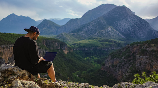 A young man works on a laptop outdoors on the mountain top, freelancer man enjoys remote work in nature.

Güver Cliff Canyon is almost a natural wonder with its rich plant diversity. It is in the borders of Düzlerçamı National Park in the Döşemealtı district. The region is preferred due to its proximity to the city center. It is one of the frequent destinations of photography enthusiasts and nature lovers with its interesting natural formations in the canyon, observation terraces and the panoramic view of Antalya.