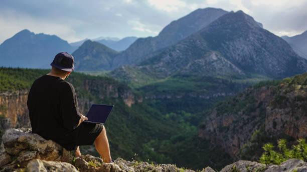 istock A young man works on a laptop outdoors on the mountain top, freelancer man enjoys remote work in nature, young man typing on a laptop on the edge of the cliff, Traveler male works outdoors using laptop, remote work alone in the mountains 1495793432
