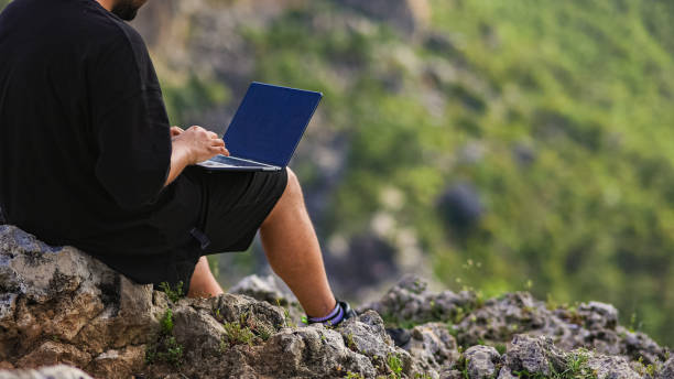 istock A young man works on a laptop outdoors on the mountain top, freelancer man enjoys remote work in nature, young man typing on a laptop on the edge of the cliff, Traveler male works outdoors using laptop, remote work alone in the mountains 1495793436