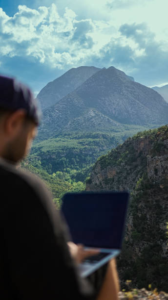 istock A young man works on a laptop outdoors on the mountain top, freelancer man enjoys remote work in nature, young man typing on a laptop on the edge of the cliff, Traveler male works outdoors using laptop, remote work alone in the mountains 1495793484